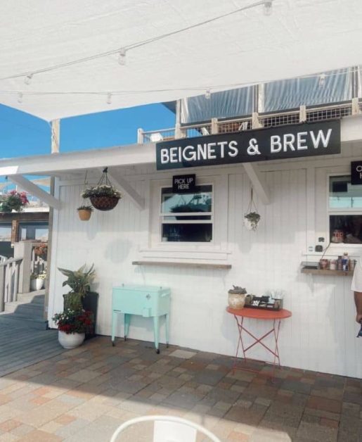 The bright white wooden exterior and light blue accents of the Beignets & Brew exterior located along the Destin Harbor.