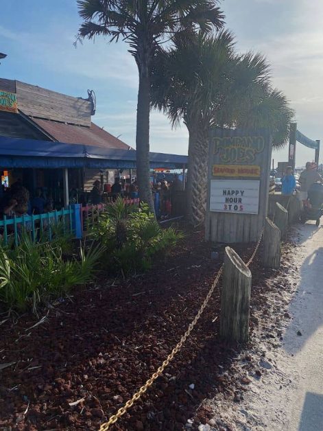 The outside of one of the best restaurants in Destin, Florida called Pompano Joes surrounded by palm trees and close to the ocean.