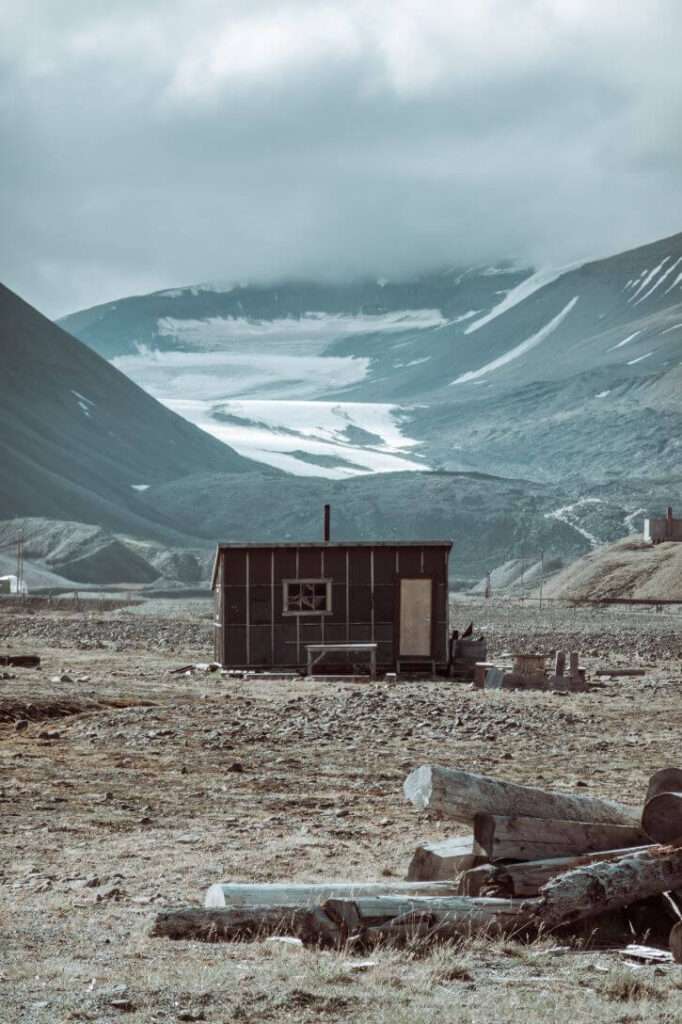The remote destination of Longyearbyen in Svalbard with one tiny shed surrounded by rugged landscape and snow covered cliff formations.