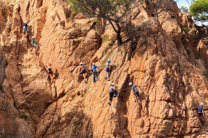 A large group of people trying out via ferrata alongside a rugged mountainside with footholds and cable sections.
