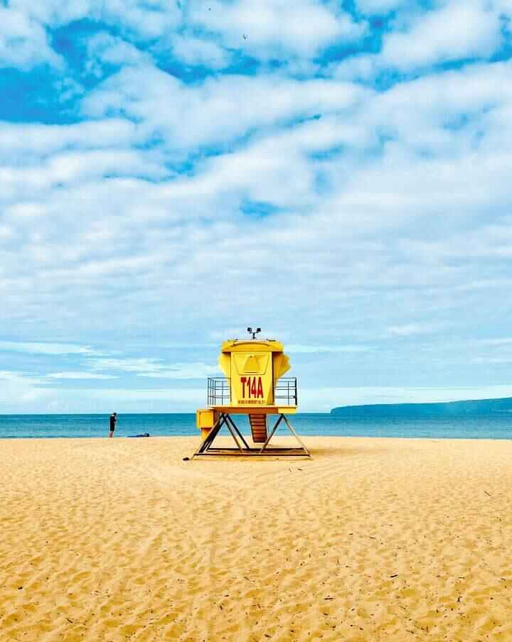 The expansive golden sand and bright blue ocean water with a large yellow lifeguard chair at Big Beach or Makena Beach in Maui.