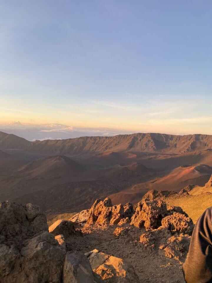 The vast volcanic landscape overlooking Haleakala National Park during sunrise with the warm orange and yellow glow of the sun. This is a cheap thing to do to lower your honeymoon in Maui cost.