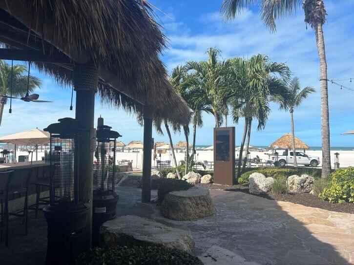 The Kane Tiki Bar & Grill at the JW Marriott surrounded by palm trees, stone paths and the beach in the distance. It is one of the best beach bars in Marco Island.