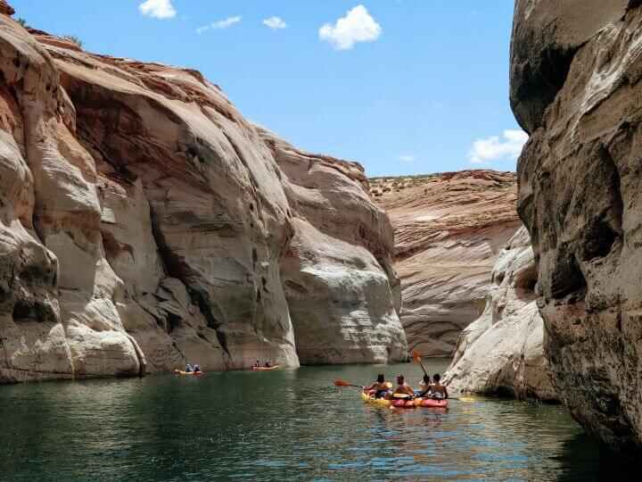 On a warm summer's day, kayakers are shown on Lake Powell surrounded by towering rock walls which is a fun thing to do along your drive from Antelope Canyon to Zion National Park.