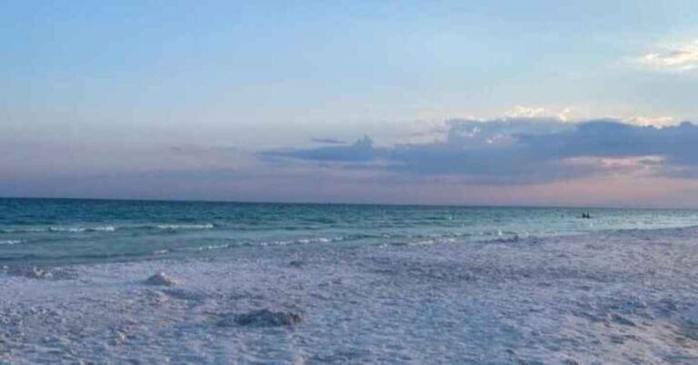 The view of the sunset at Miramar Beach near 30A Florida with the sky showing colors of pink over the emerald blue water of the ocean and white soft sand.