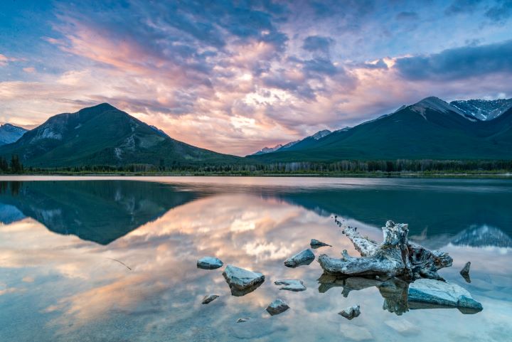 The beautiful orange and pink sunset casting behind the mountains while the mountains reflections are shown in the water at Vermilion Lakes which is why it is one of the best lakes in Banff.