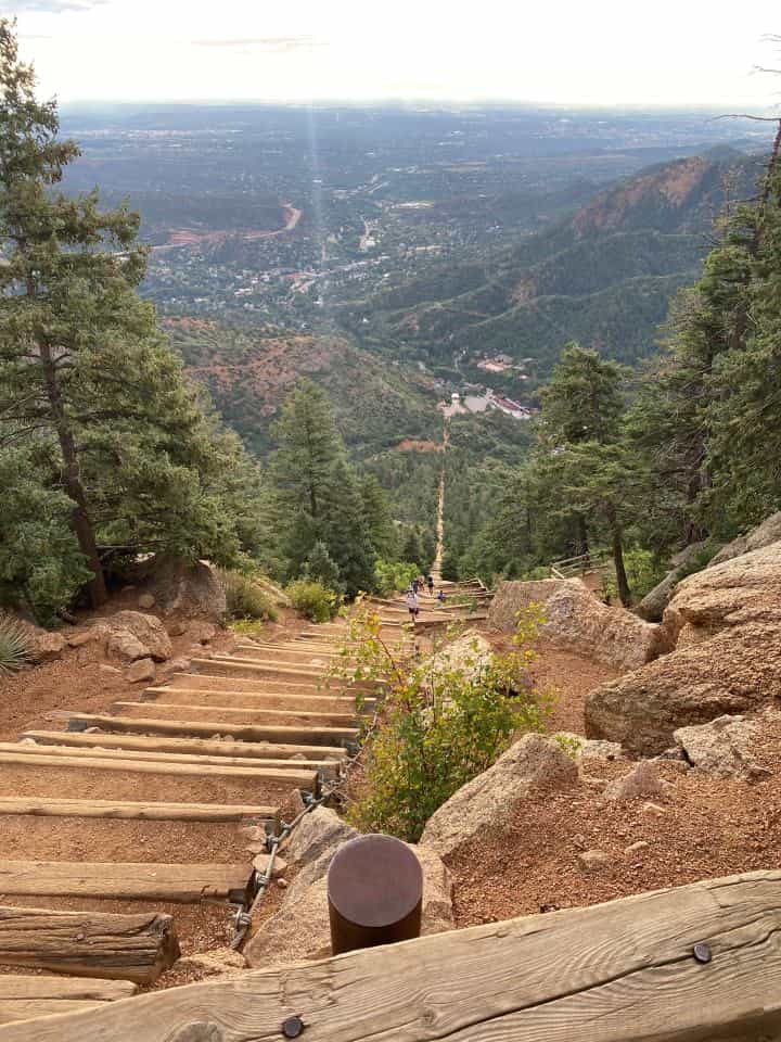 People ascending the steep set of stairs of the Manitou Incline while you can turn around and overlook the mountains and Colorado Springs.