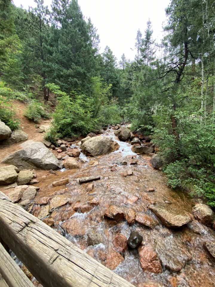 The North Cheyenne Creek flowing underneath a bridge surrounded by rocks and tall skinny trees during the Seven Bridges hike in Colorado Springs.