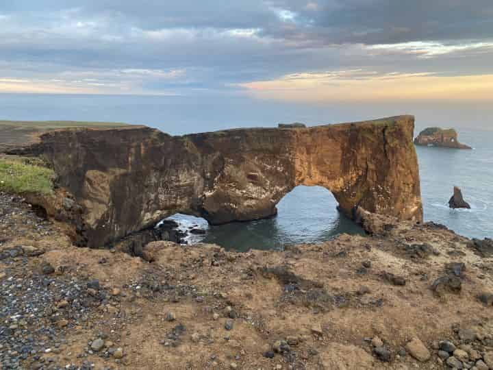 The beautiful sunset casting an orange glow in the sky behind the Dyrholaey Arch which is a unique rock formation extending over the cliff and ocean and is near Vik in Iceland.