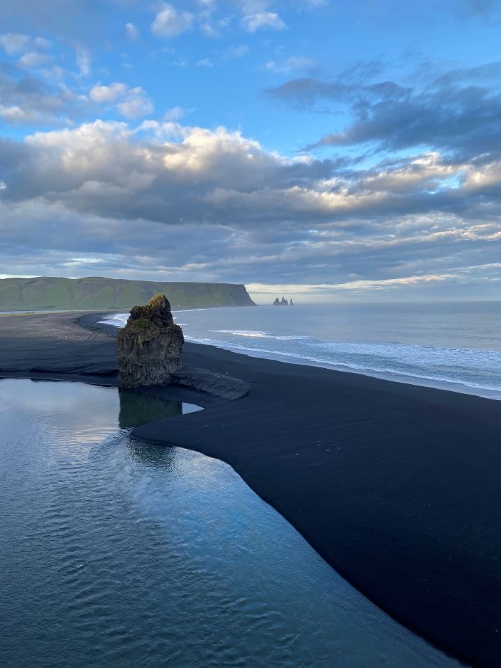 A large black rock formation surrounded by the ocean and black sand at Reynisfjara Black Sand Beach in Iceland.