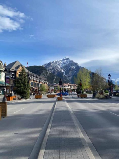 The view of a large mountain covered with snow that you can see from the main street in downtown Banff while being surrounded by restaurants and shops.