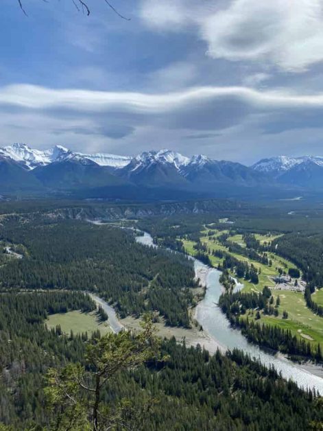 The beautiful views you can see while hiking Tunnel Mountain in downtown Banff which gives you views of the snow-covered mountain range, clear blue bow river, and dark green fir trees.