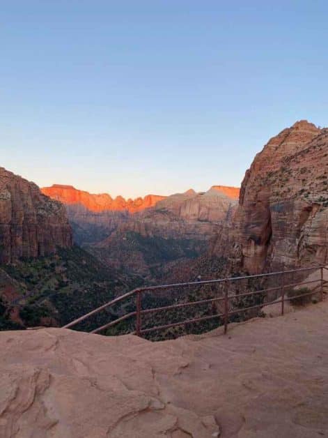 The view of the orange glow of the sunrise casting over the red rock canyon walls on Zion Canyon Overlook trail in Zion National Park.