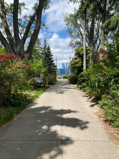 The view of the Toronto skyline while you walk down a residential street full of homes on Algonquin Island on Toronto Islands.