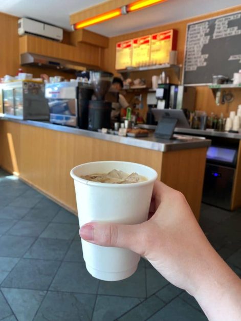 The retro-style vibe of the inside of Made Rite coffee shop in Toronto with me holding up my vanilla iced latte.