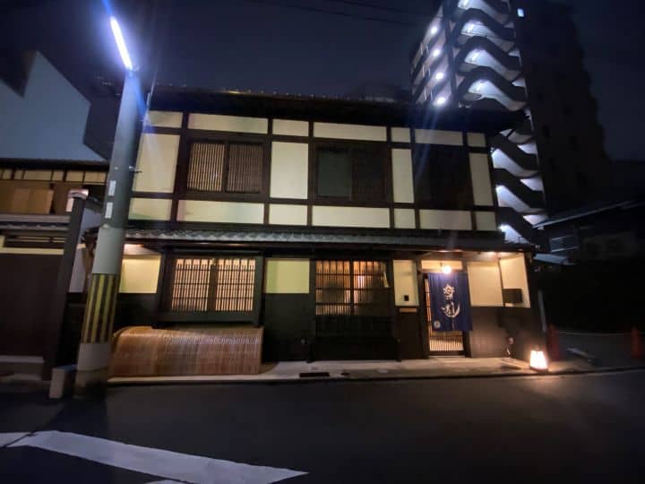 The traditional exterior of Luck You ryokan in Kyoto at night illuminated with the warm glow of the lamps outside.