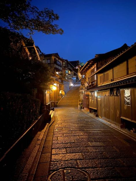 Ninenzaka street in the historic Higashiyama district in Kyoto lit up at night with the warm glow of lanterns lining the sloped stone streets.