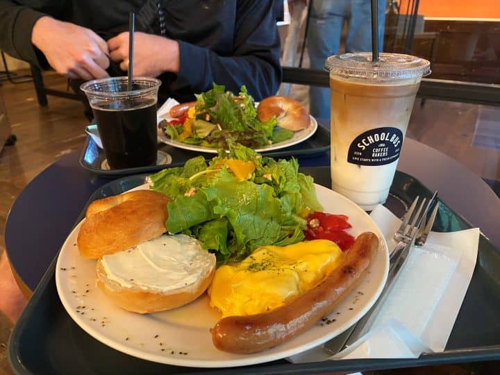 The breakfast plate at School Bus Coffee Bakers in Kyoto which consists of a bagel, salad, eggs, and sausage as well as a large iced latte.