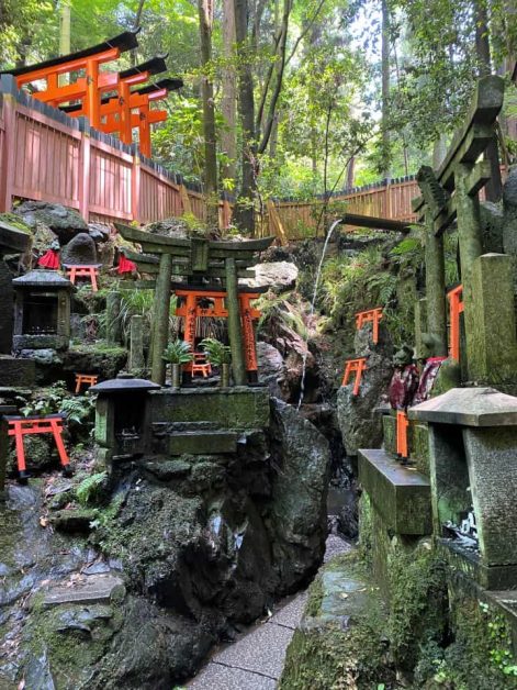 A small shrine off the main path while hiking to the top of Fushimi Inari Taisha surrounded with small red torri gates and water spouts.