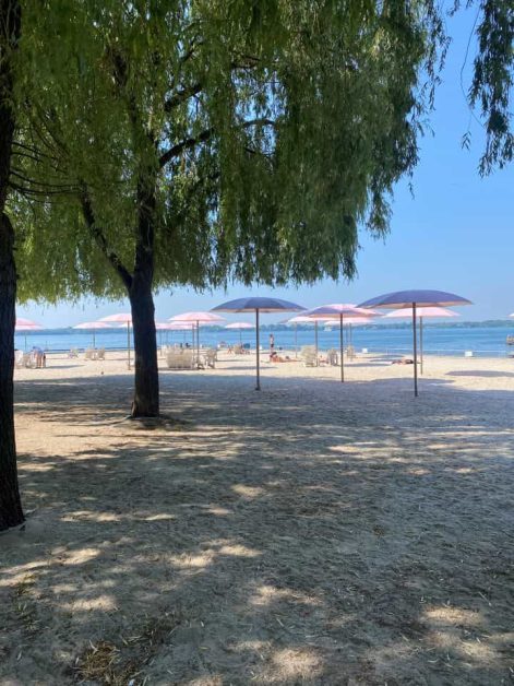 The pink umbrellas, beach chairs, and tan sand at Sugar Beach which is a small urban park near the waterfront of Lake Ontario which is perfect for sunbathing in Toronto