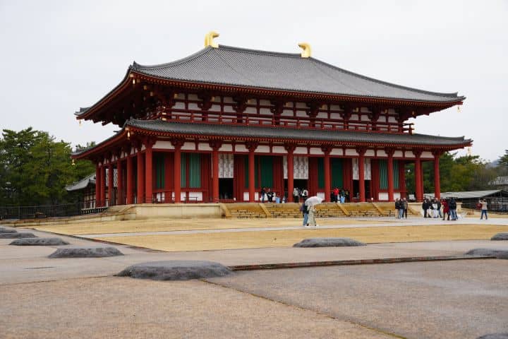 Kofuku-ji Temple in Nara Japan with visitors walking in front of the historic red wooden building.