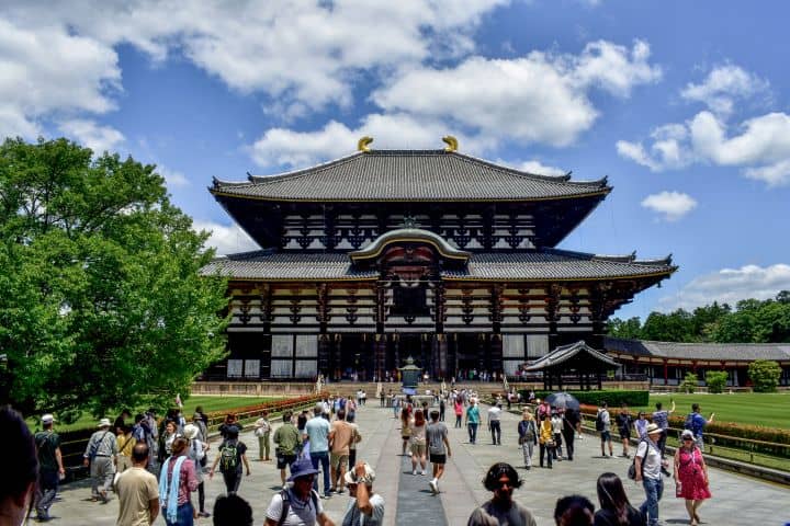Todai-ji Temple in Nara Japan with crowds walking toward the main hall under a blue sky.