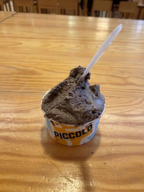 A small cup of cookies and cream gelato with a plastic spoon, that sits on a wooden table at Time Out Market.