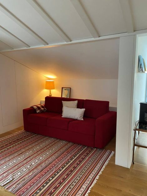 Cozy living room with a red sofa, white and plaid cushions, a patterned rug, and a warm table lamp in our 2-bedroom apartment at The Lisboans.