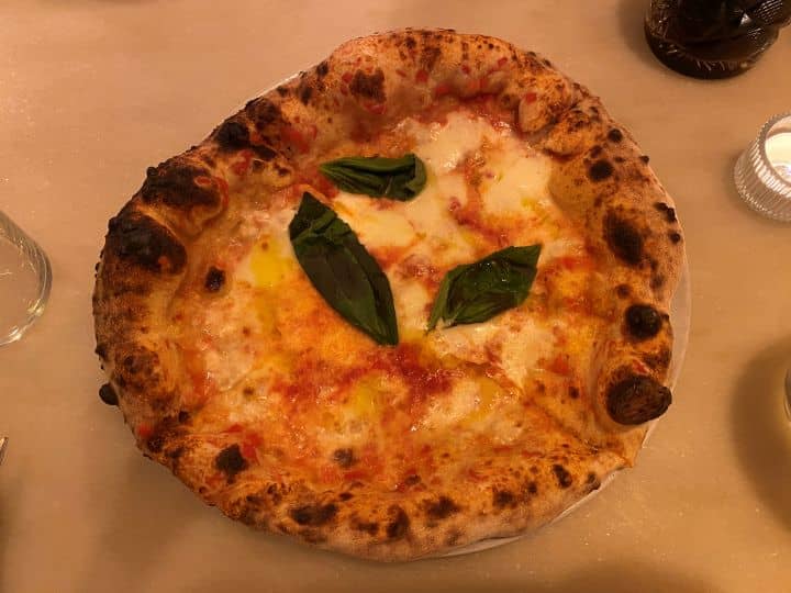 Wood-fired Margherita pizza with charred crust, melted cheese, tomato sauce, and fresh basil leaves served at Pizzico Pizzeria restaurant in Lisbon.
