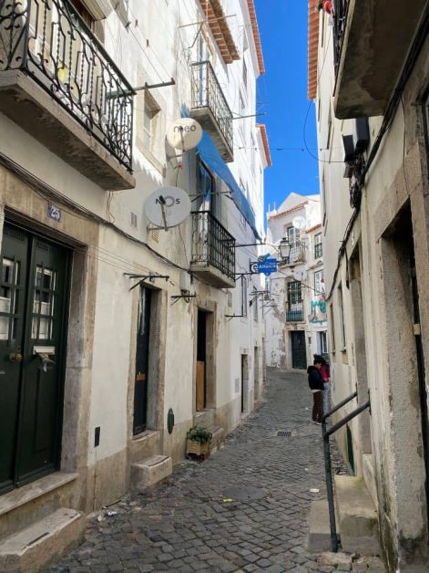 Narrow cobblestone street in Lisbon, lined with historic buildings and balconies.