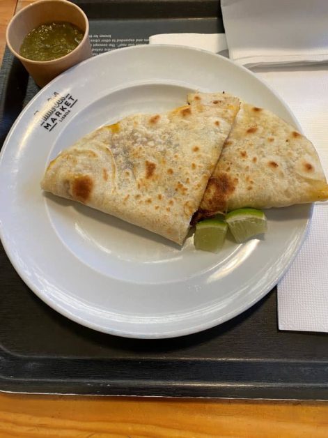 A steak quesadilla served with salsa verde and lime wedges from a food vendor at Time Out Market in Lisbon.