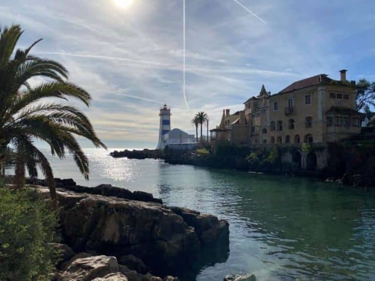 The blue and white striped Santa Marta lighthouse in Cascais you can see along the water near the palm trees.
