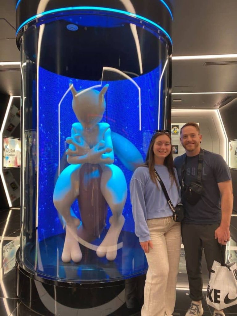 My husband and I standing in front of the large Mewtwo statue at the Pokemon store in Shibuya which is a popular area to visit on a 3-day Tokyo itinerary.