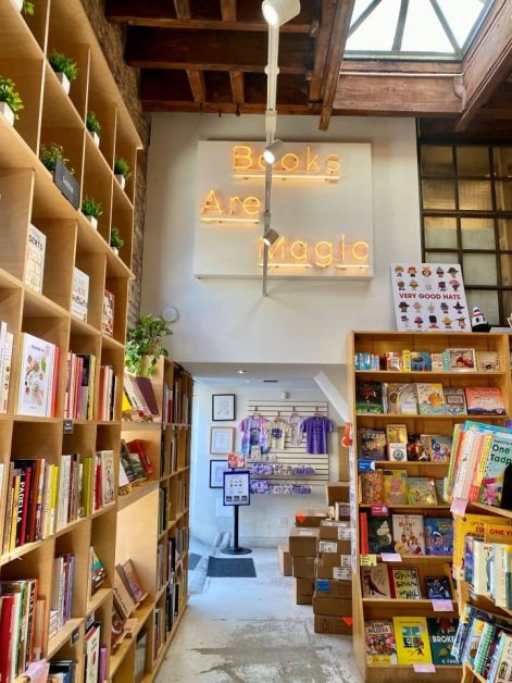 The inside of the Books are Magic store in Brooklyn along with a neon sign and rows of books.
