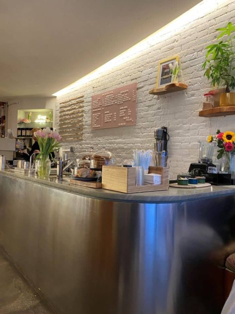 The interior of Enly coffee shop in New York City with a light pink menu board and white brick wall.