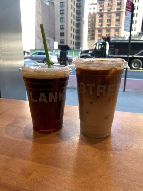 Two iced coffees, a blondie and cold brew, on a table with a city view from Blank Street coffee shop in NYC.