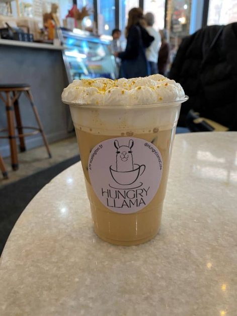 A whipped honey latte from Hungry Llama coffee shop in New York City, topped with thick cold foam and a fun sticker.