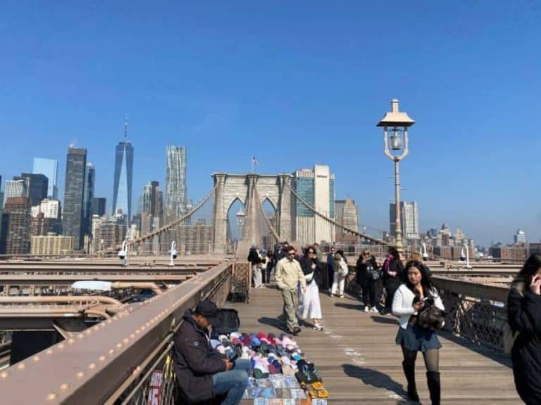 The views of the Manhattan city skyline in the background while you walk across the Brooklyn Bridge to enter Brooklyn.