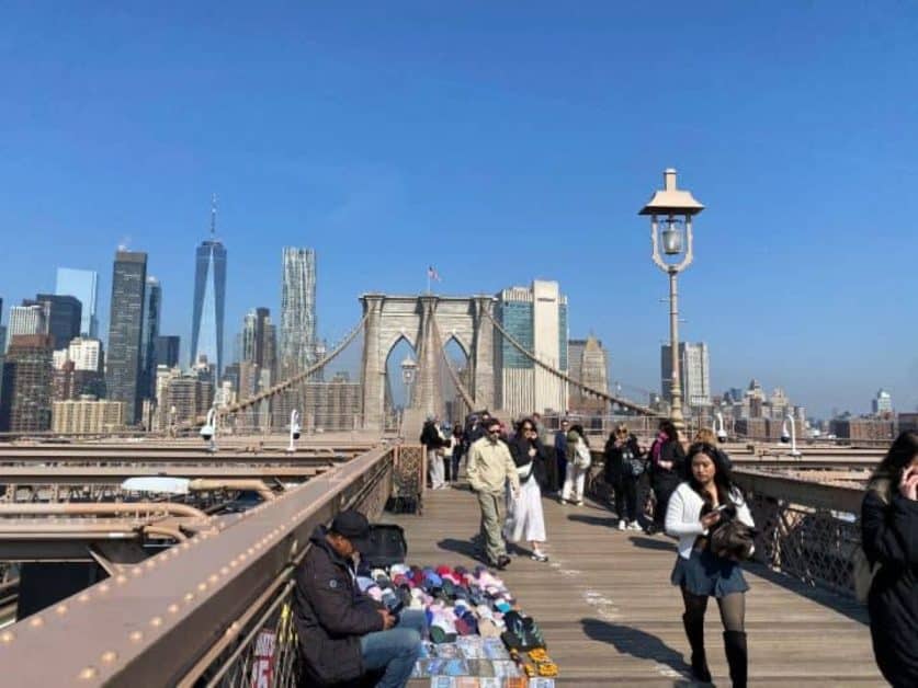 The views of the Manhattan city skyline in the background while you walk across the Brooklyn Bridge to enter Brooklyn.
