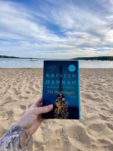 Holding up a copy of The Nightingale by Kristin Hannah on Riviera Beach in Lake Geneva, Wisconsin.
