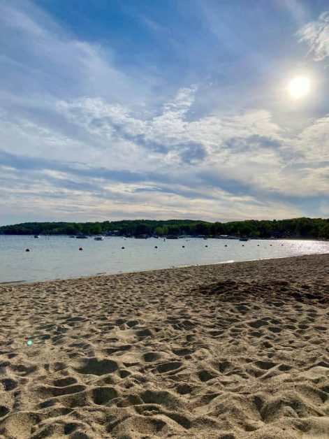 Sandy shoreline and sunlit water dotted with boats at Riviera Beach in Lake Geneva, Wisconsin.
