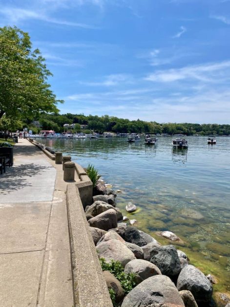 Rocky shoreline and walking path along Lake Geneva, Wisconsin, with boats on the water.