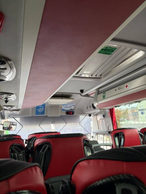 Interior of a coach bus with red leather seats, looking toward the ceiling with luggage racks, WiFi and USB charging signs, and a digital speed display reading 75.