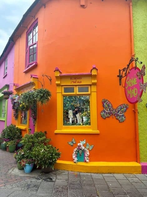 Close-up of the vivid orange "Stone Mad" shop front with a yellow-framed window display, pink signage, and decorative butterflies on the wall.