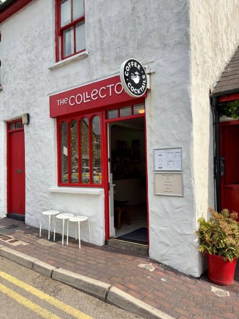 White building with red trim and doors, signage reading "The Collector, Coffee Cocktails," with small white stools outside and a potted plant by the entrance.