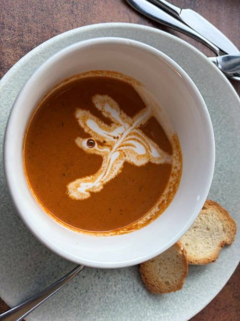 Overhead view of a bowl of orange lobster bisque with a decorative cream swirl, served with toasted bread slices.